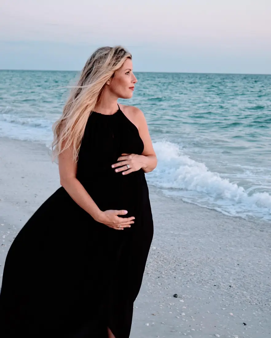 Expecting mother in a black dress gazing out at the ocean