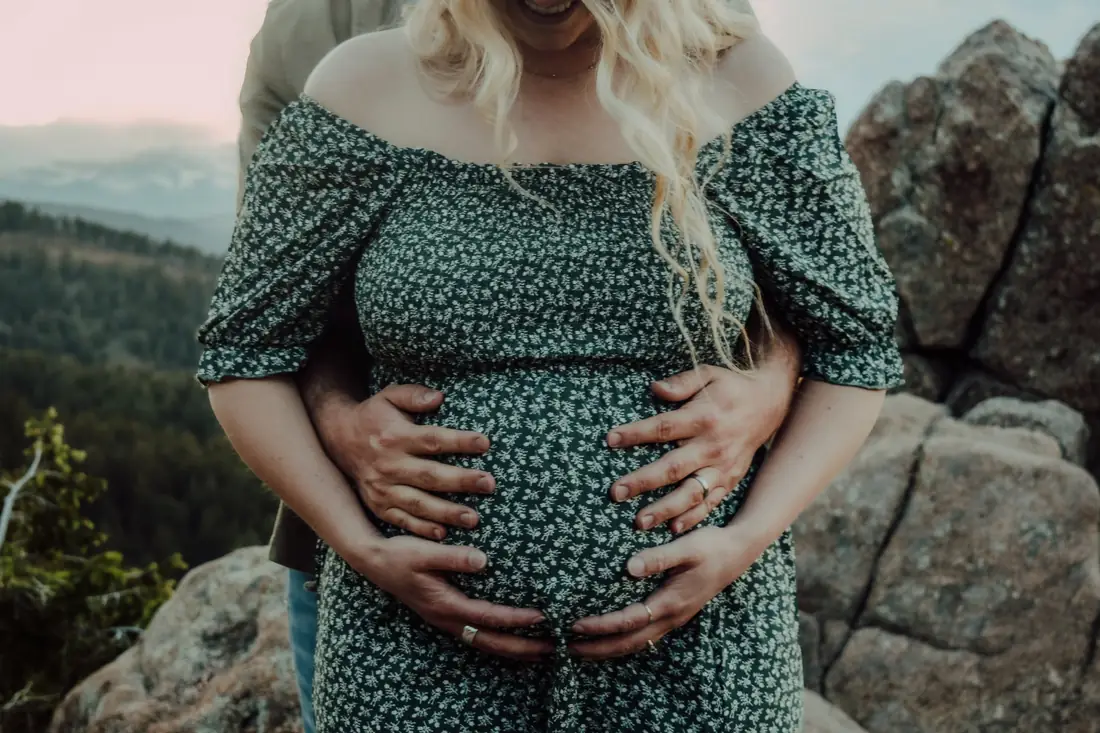 Close-up of a couple's hands on an expecting belly at a mountain overlook