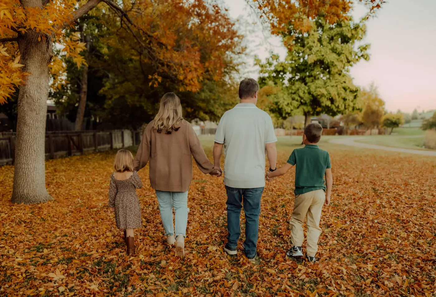 Family of four holding hands walking away through fallen autumn leaves