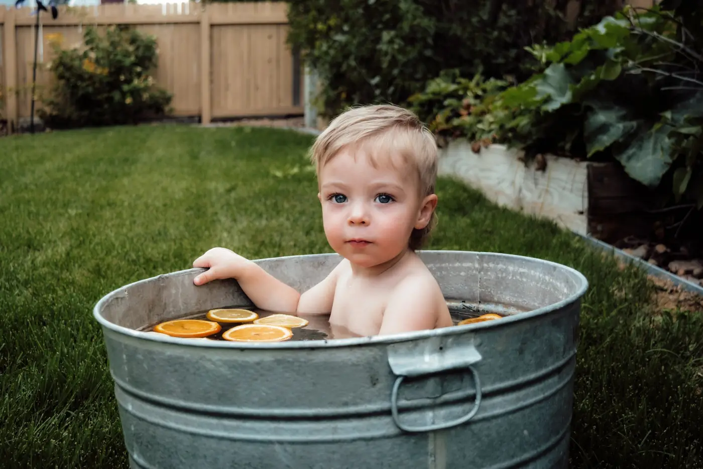 Toddler with blue eyes sitting in a tub of orange slices in the backyard