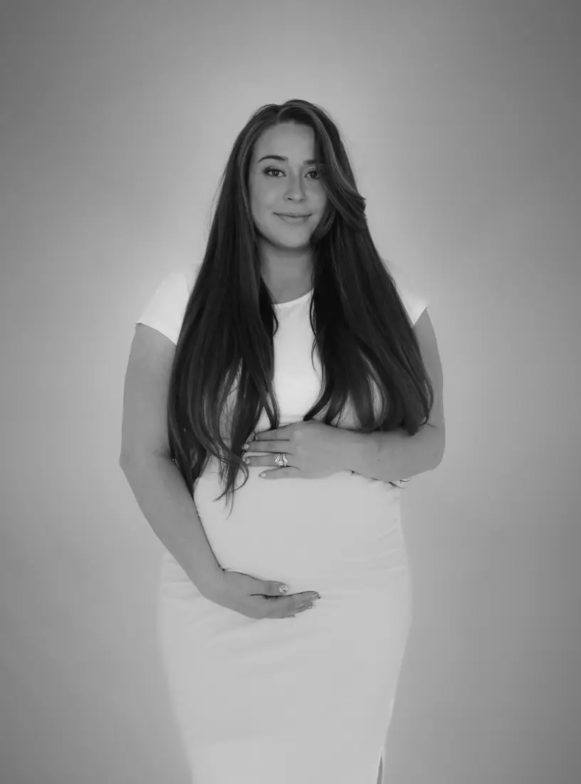 Black-and-white studio maternity portrait in a white dress
